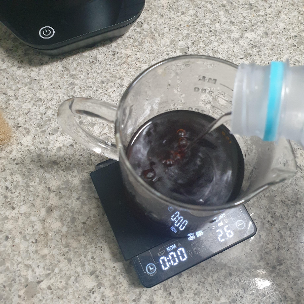 저울위에 추출한 커피가 있고 PET 물병으로 상온수를 따르는 모습