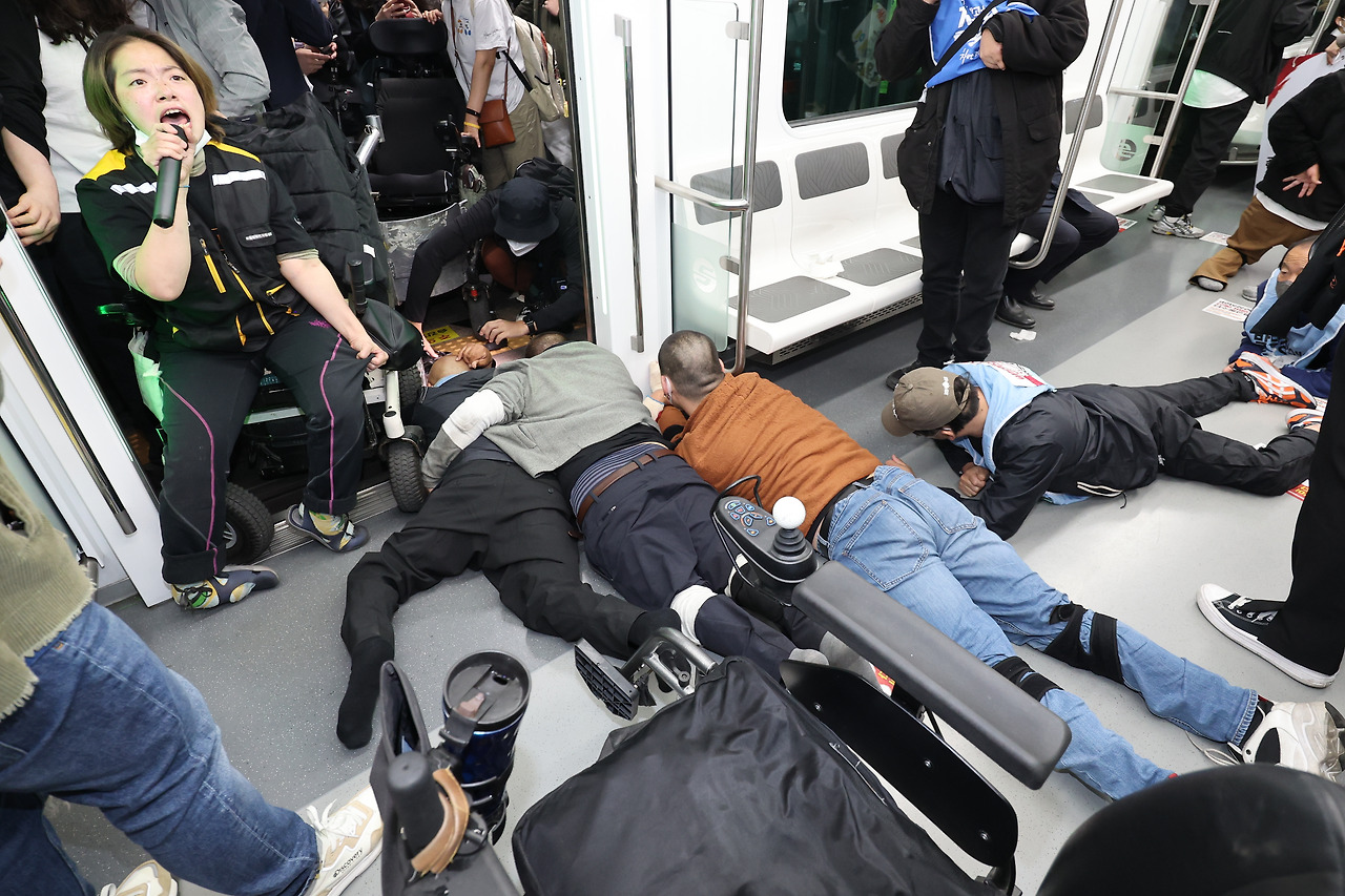 21일 오전 서울 지하철 2호선 시청역에서 전국장애인차별철폐연대(전장연) 관계자들이 출근길 지하철 탑승 시위를 하고 있다. 일부는 차량 문 앞에 휠체어를 세우고 문이 닫히지 않도록 했고, 몇몇은 ‘오체투지’(사지와 머리를 바닥에 대고 엎드리며 절하는 것)를 하며 바닥을 기듯 열차 내부에서 몸을 움직이는 방식으로 시위를 했다./연합뉴스