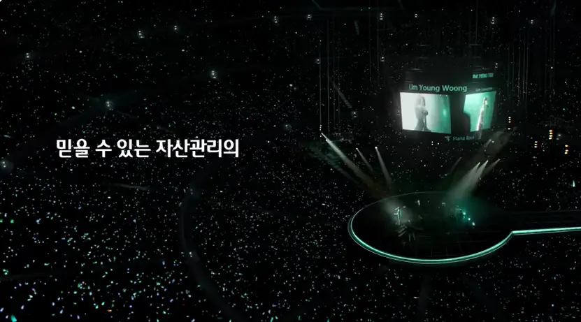 임영웅- 검은 무대 불빛들이 반짝이는 콘서트 장 좌측 흰글씨 믿을 수 있는 자산의 화면 우측 무대를 멀리서 찍은 사진