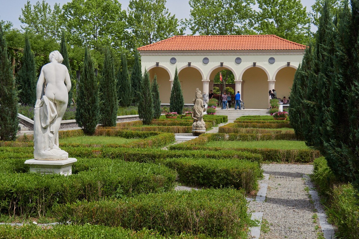 Clipped hedges and a marble statue in front of an arcaded pavilion in a formal garden at Suncheon Bay National Garden