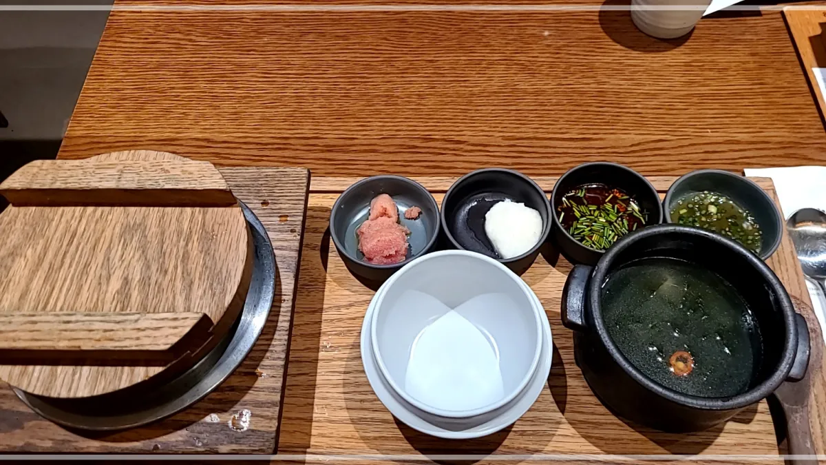 나무테이블위 밥상 나무뚜껑이 닫힌 영양밥솥, 빈그릇, 미역국, 명란젓, 무즙, 양념간장, 고추물