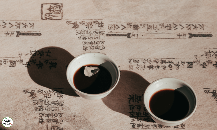글자가-적힌-한지로-덮힌-책상-위에-한약이-담긴-사기잔-2개가-놓여져있음