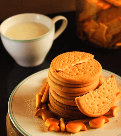 하얀 접시에 둥그런 비스킷들이 쌓여있고, 접시 뒤에는 하얀 컵에 우유가 가득하다.