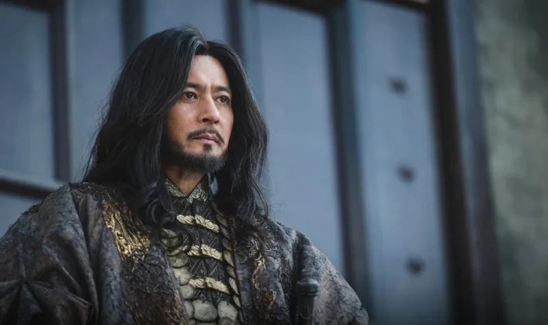 거대한 철문을 배경으로 화려한 왕의 복장과 긴 머리를 내려 트리고 위엄있게 앉아 있는 아라문의 검의 타곤 캐릭터