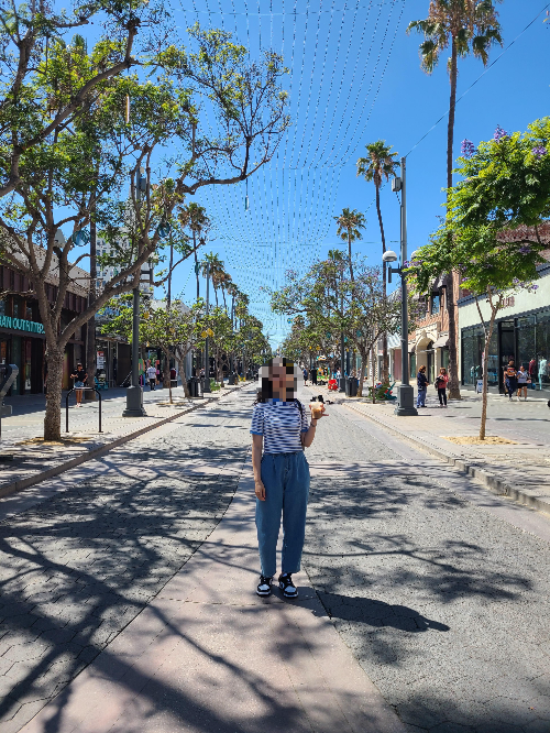 다운타운 산타 모니카 거리의 모습. 양쪽으로 쇼핑몰과 나무가 한 줄로 서 있다. 왼쪽에는 스타벅스가 보인다. 스타벅스에서 산 커피를 들고 길의 가운데 서서 사진을 찍었다. 