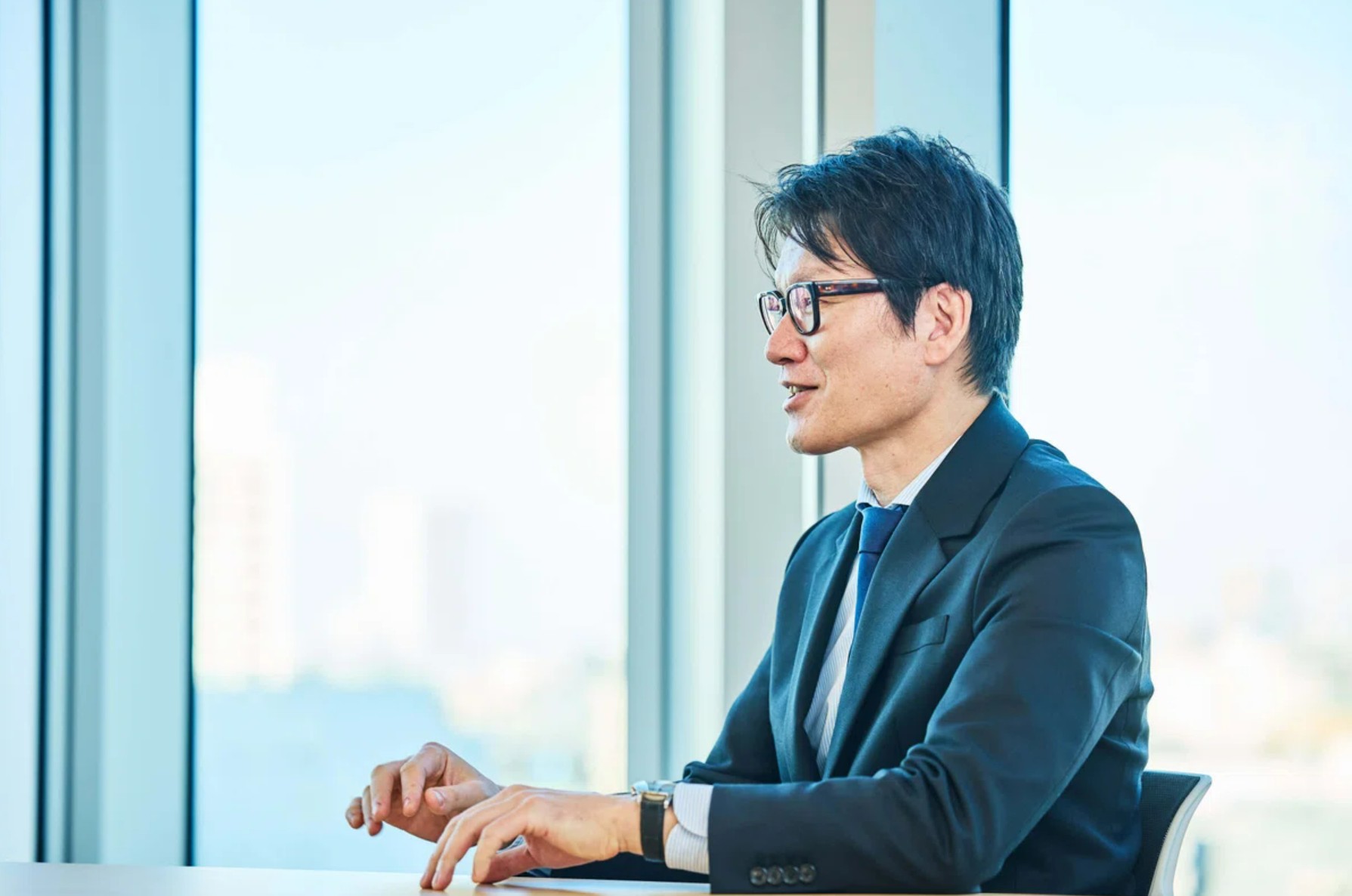 외야마의 상반신 사진(옆얼굴). 사무실 유리창을 배경으로 이야기하는 모습이다.