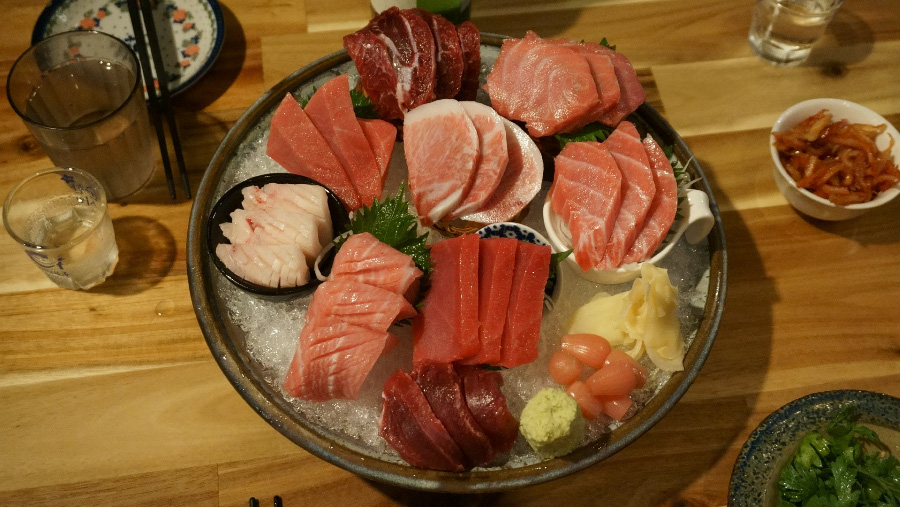 바다에서 채취를 한 참치를 잘 손질해서 회로 만들어 동그란 항아리 뚜껑 접시에 얼음을 깔고 그 위에 참치회를 종류별로 놓아두고 그 주변에 여러가지 밑반찬을 놓고 찍은 사진