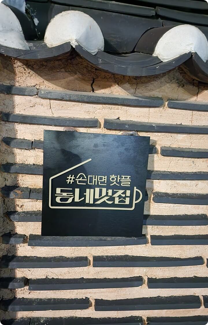 기와 지붕이 있는 벽에 '손대면 핫플 동네멋집'이라고 적힌 간판