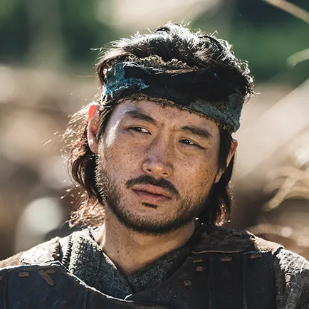 수염이 난 30대 남성이 이마에 천으로 머리를 두르고 무복에 갈색 가죽 갑옷을 입고 있는 아라문의 검 바로루 캐릭터