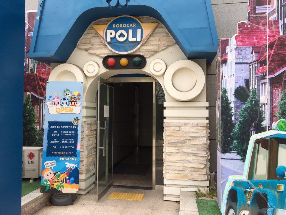 로보카 폴리 키즈카페 입구, 파란 지붕, 신호등 장식. 운영 시간 안내판이 옆에 있음.