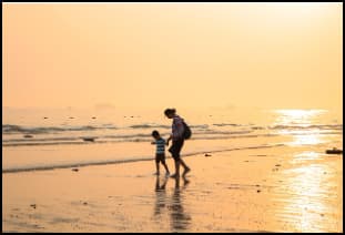 노을 진 해변을 손잡고 걷는 엄마와 아이의 평온한 순간