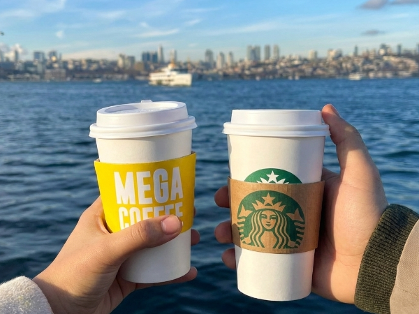 바다가가 보이는 곳에서 메가 커피와 스타벅스 커피를 들고 있는 모습