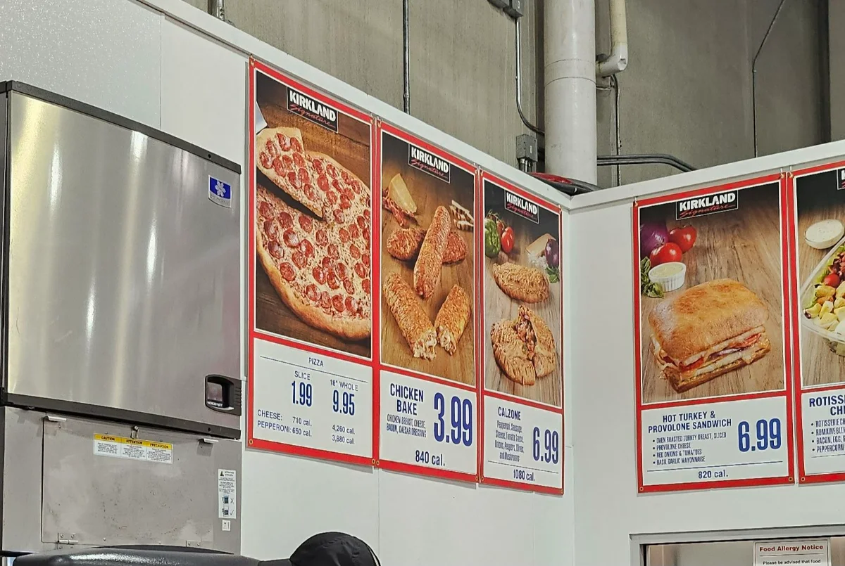 Costco food court menu board showing pizza slice $1.99, chicken bake $3.99, calzone $6.99