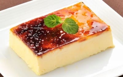 흰색 접시 위에 노란색 푸딩이 올라가 있다. 푸딩의 위에는 짙은 갈색의 소스와 녹색 파슬리가 올라가 있다.