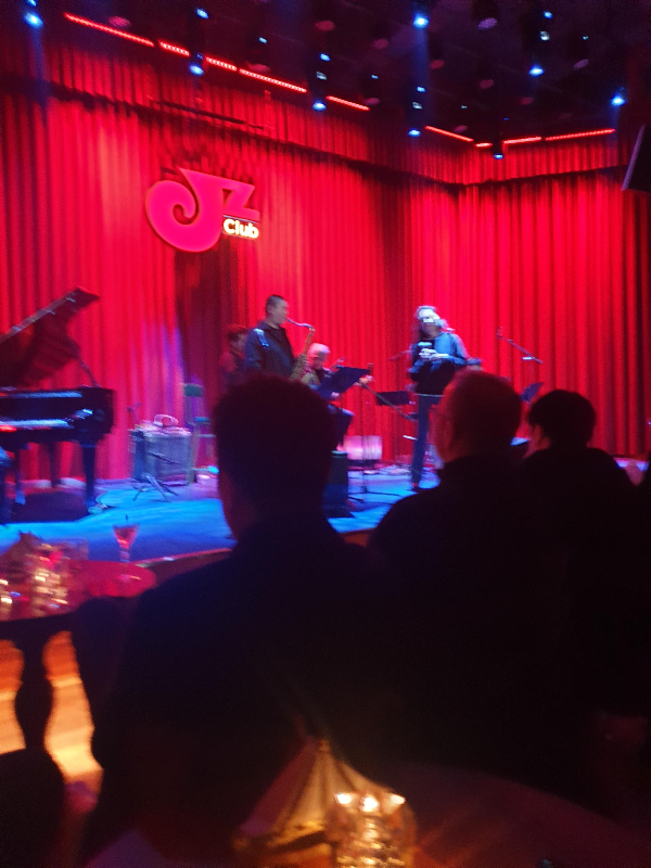 무대에는 재즈 밴드가 공연을하고 사람들은 이를 지켜보고 있다.