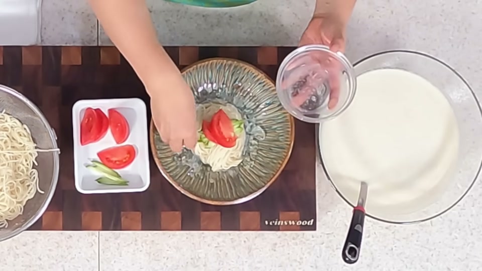 그릇에 중면과 콩물을 담고 토마토·오이를 올리는 장면