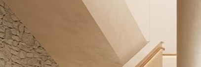 따뜻한 베이지 톤의 미니멀한 실내 공간과 통유리창 너머 푸른 정원이 조화를 이루는 브랜드 플래그십 스토어의 전경입니다. 원목 테이블 위의 커피 한 잔과 세련된 계단 구조가 여유롭고 지적인 라이프스타일의 분위기를 자아냅니다.