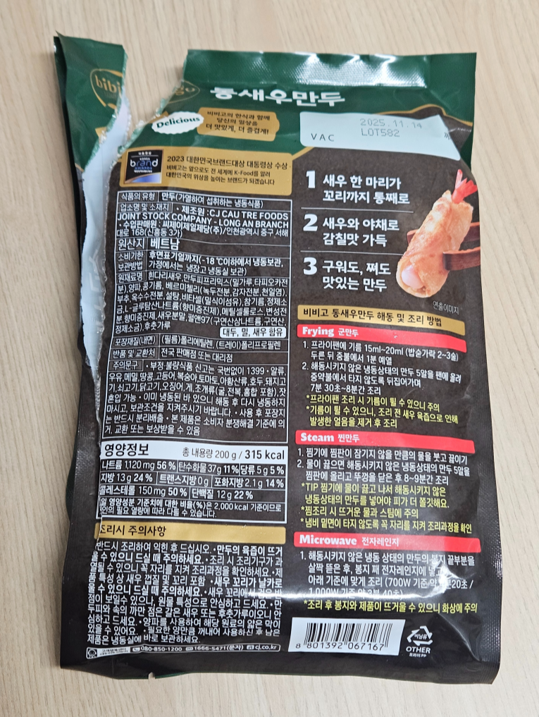 비비고 통새우만두 제품의 뒷면 포장지 사진으로, 새우 비주얼과 제품정보가 든 패키지가 테이블 위에 놓여져 있음