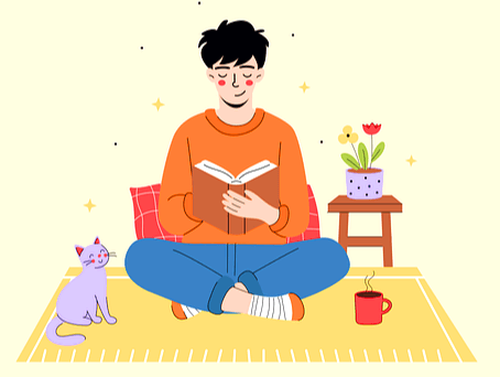 검정머리 젊은 남자가 주황색 스웨터를 입은채 방에 앉아서 책을 읽고 있다. 양 옆에는 꽃화분과 고양이가 있다.