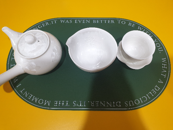 다관 공도배 찻잔이 촤측부터 놓여있다. 노란색 테이블 위 테이블 매트 위에 있다.