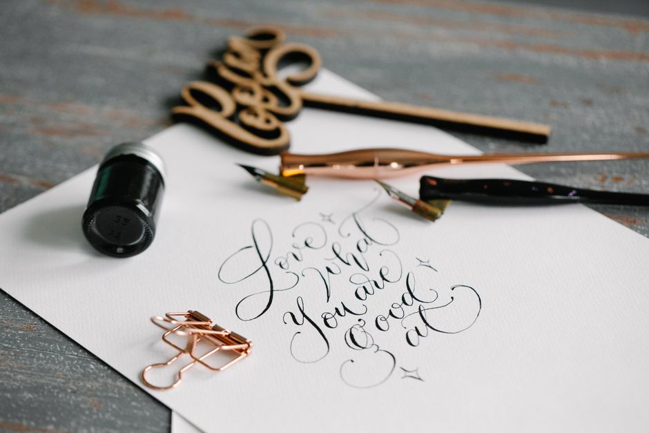 Close-up of elegant calligraphy text 'Love what you are good at' with ink and dip pen on white paper.