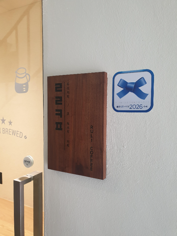 벽면에 블루리본과 작은 목간판이 달려있다. 목간판에는 ㄹㄹㅋㅍ과 초럭셔리 커피라는 문구가 보인다.