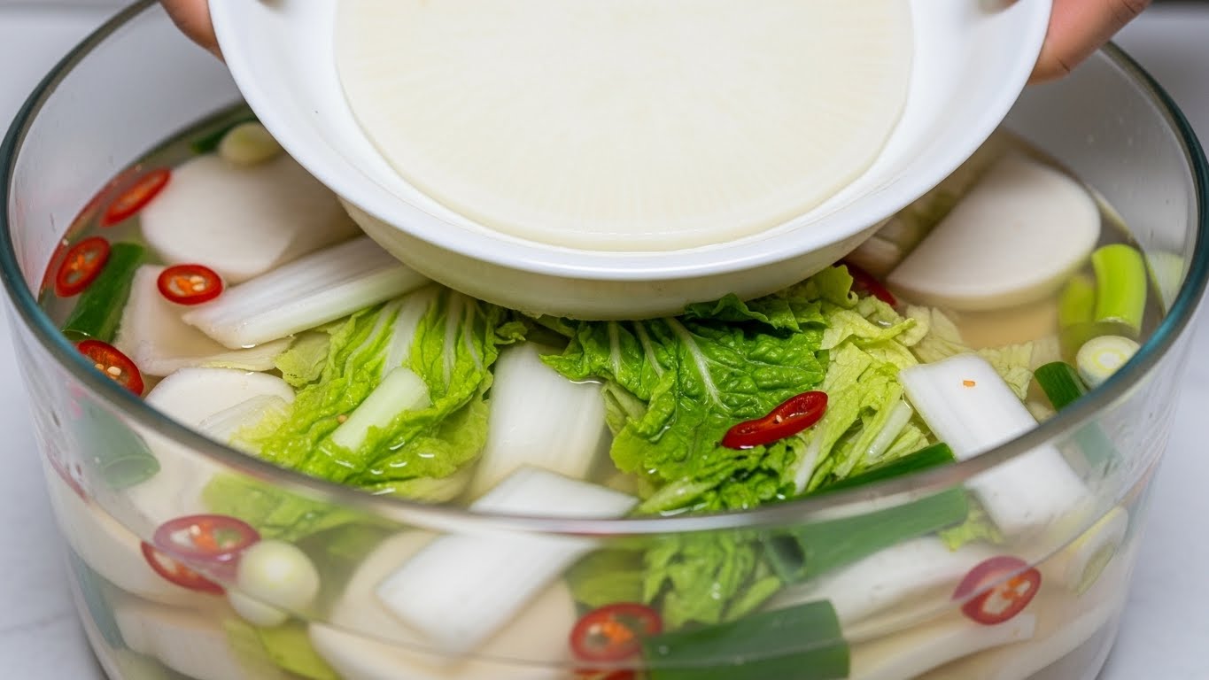 맑은-국물,-무-조각,-배-조각,-고추가-부드럽게-떠-있는-아름다운-스타일의-동치미-그릇이-한국식-나무-테이블-위에-있습니다.