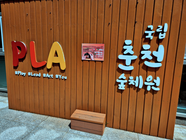 나무 벽면에 부착된 PLA 로고와 국립춘천숲체원 글자