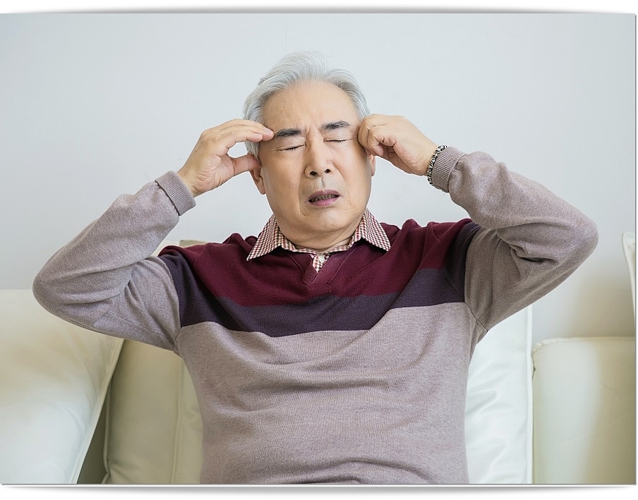 양쪽 관자놀이 부근을 두 손으로 붙잡고 다소 괴로운 표정을 짓고 있는 남성 노인의 모습