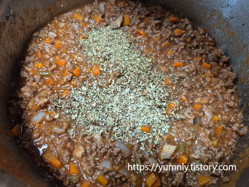 Sprinkling a generous amount of dried oregano over the simmering ragu sauce