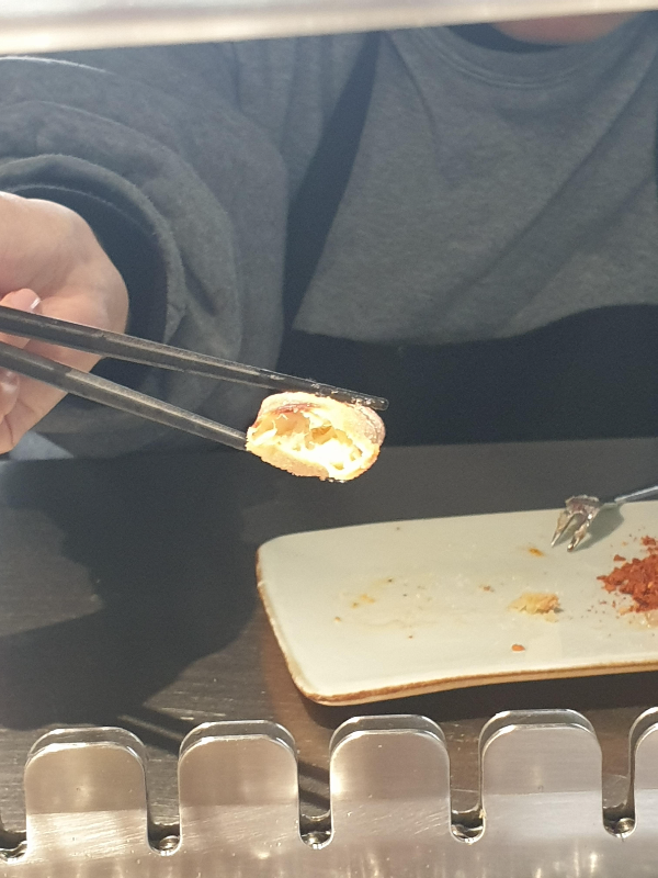 젓가락으로 고기 한 점을 든 모습. 접시 위에 시즈닝과 꼬치를 빼는 도구가 보인다.