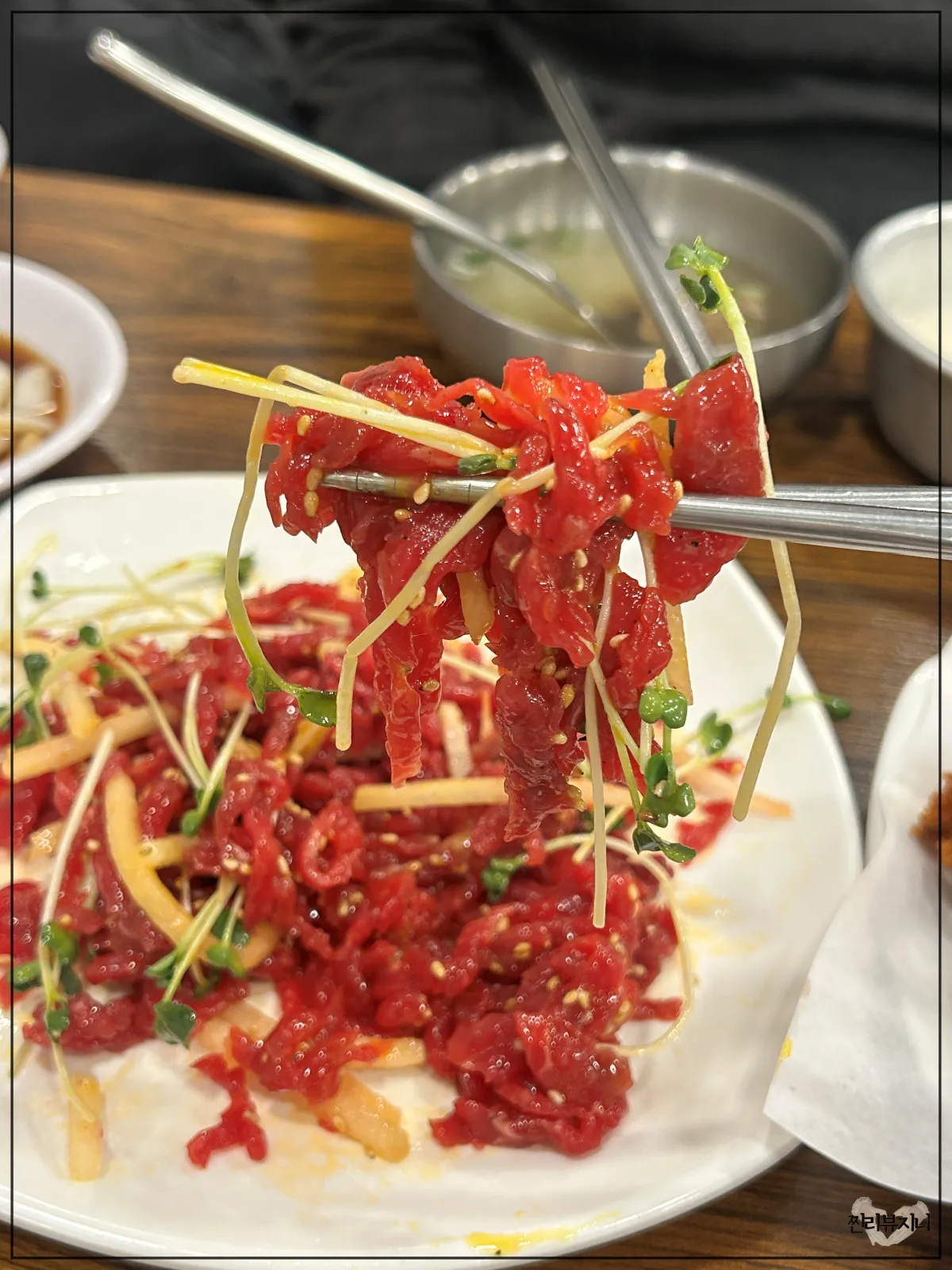 종로-통큰누이네-육회빈대떡-메인-메뉴-누이네-세트-중-육회를-젓가락으로-들고있는-모습