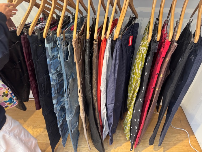 ⁠A metal rack filled with various Supreme pants, cargo jeans, and ripstop trousers inside the boutique⁠