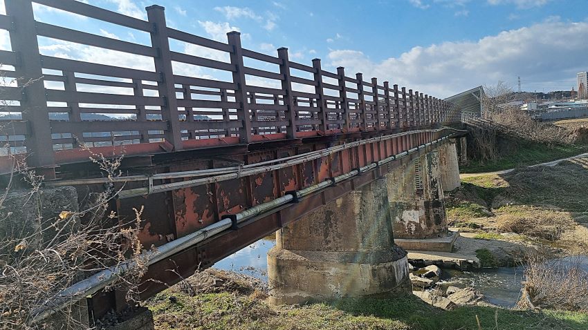철교의 비스듬한 옆 모습, 육중힌 상판에 놓인 철판, 육중한 콘크리트 교각, 좌우로 흐르는 실개천, 푸른 하늘 흰구름,