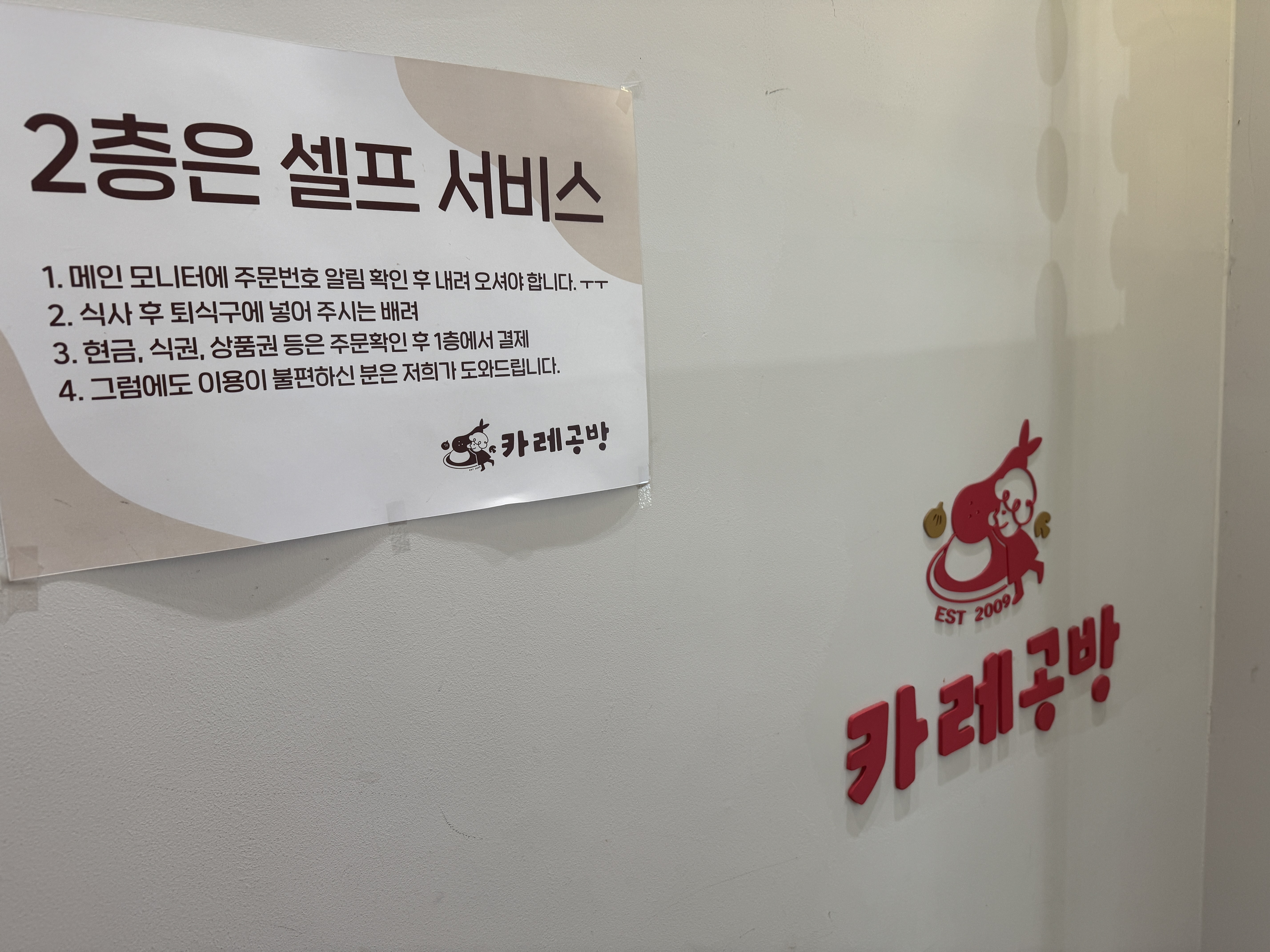서현 카레공방 2층 셀프 서비스 안내문 &ndash; 주문 확인&amp;#44; 퇴식구 이용&amp;#44; 1층 결제 안내가 적힌 벽면 공지