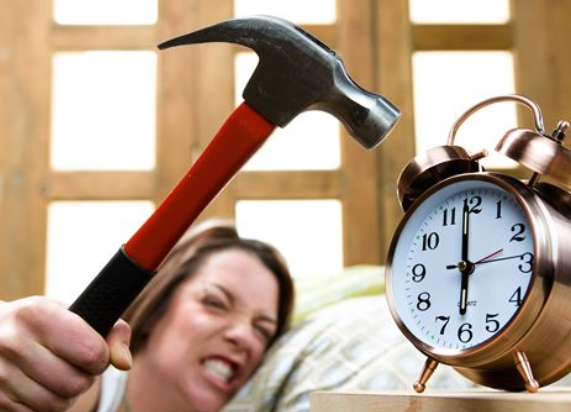 침대에 누워 망치로 알람시계를 부술려고 하는 여인