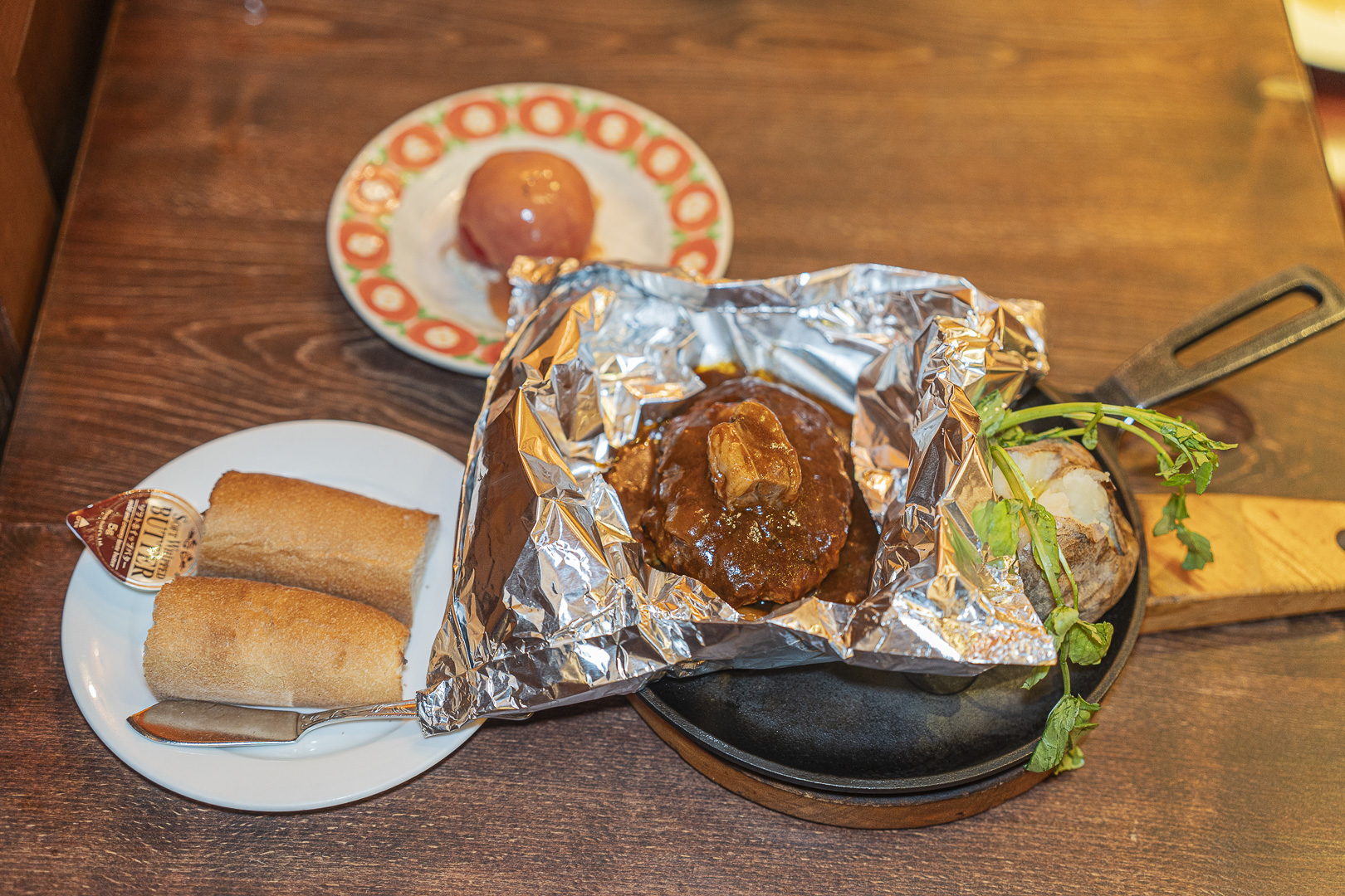 Grill Capital Toyotei, Kyoto Porta: a sauced hamburger steak on an iron plate inside opened foil, with potato, bread and tomato alongside.