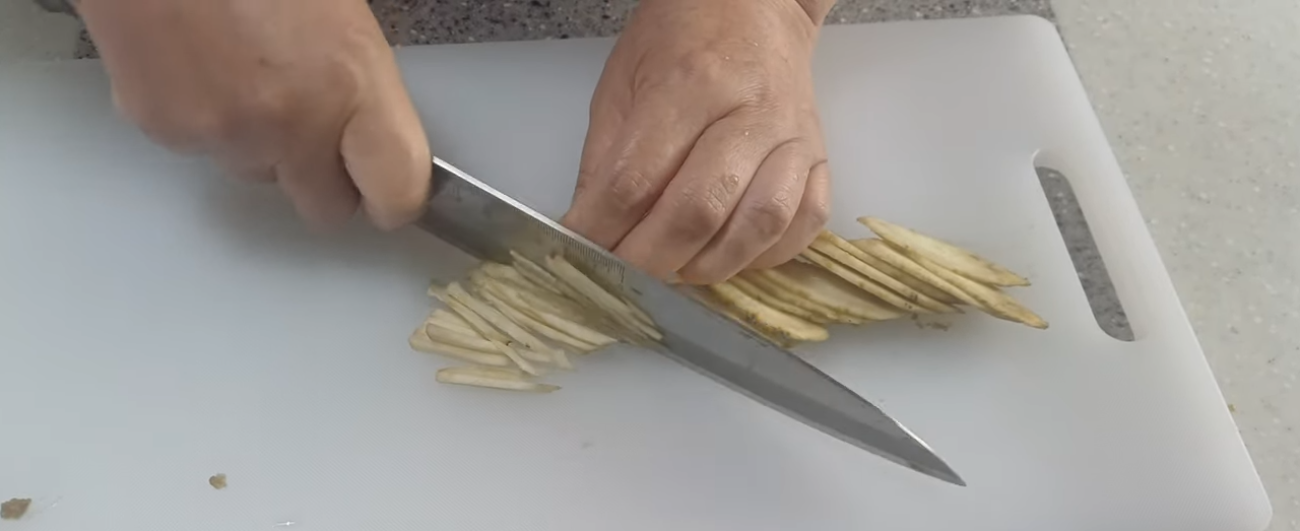 칼로 우엉을 어슷하게 썬 뒤 가늘게 채 써는 모습