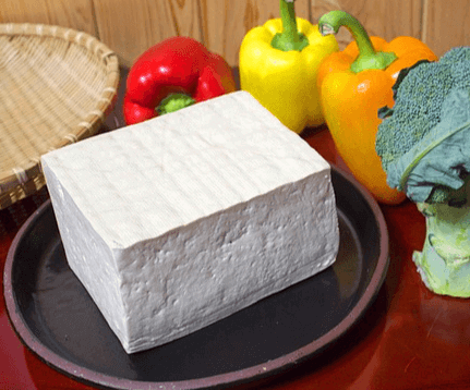 도자기 접시에 하얀 두부 한 모가 있다. 주변에는 빨간 파프리카와 노란 파프리카가 있다.