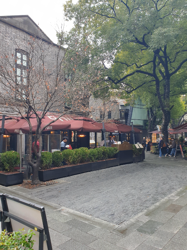 회색 벽돌 건물 앞에 붉은 어닝으로 된 야외 좌석이 배치되어 있다.