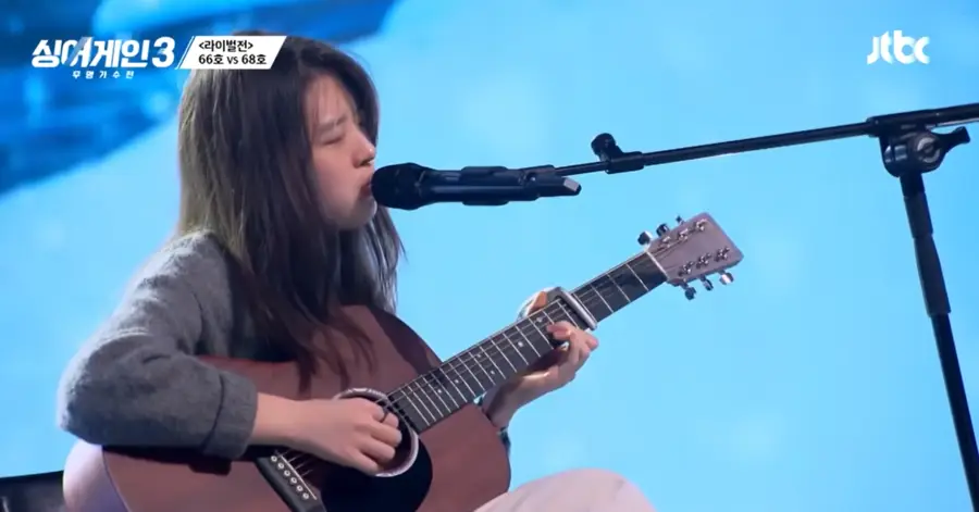 싱어게인3-
갈색기타를 치며 회색 스웨터를 입고 긴머리를 늘어뜨린채 스탠딩마이크 앞에서 노래하는 68호 우측 옆모습