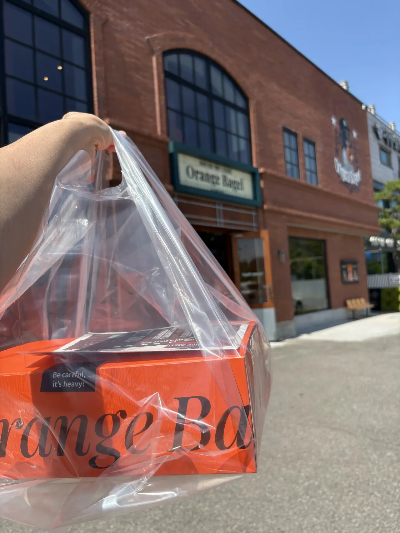 오렌자-베이글-건물-앞-베이글-선물상자-들고있는-손