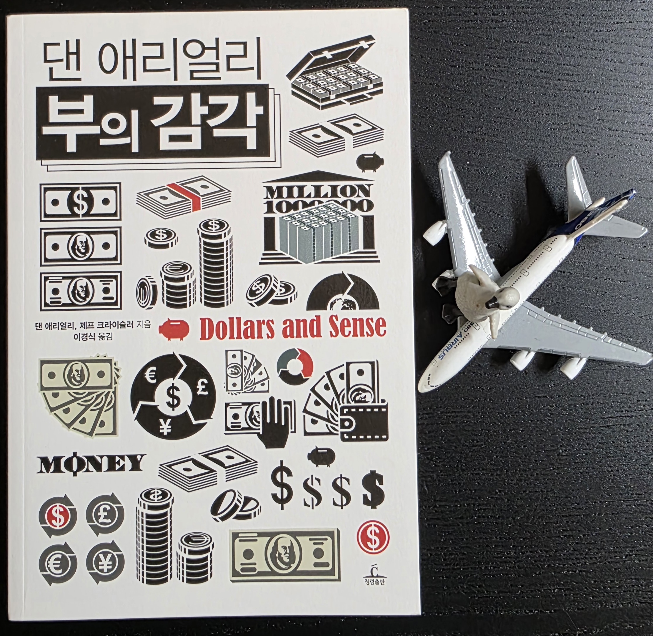 비행기 모형을 탄 펭귄 피규어와 댄 애리얼리 부의 감각 책 표지