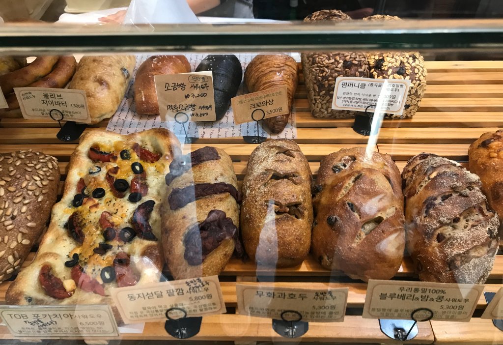 진열대에 있는 포카치아, 동지섣달 팥깜빠뉴, 무화과 호두 사워도우, 블루베리 밤 콩 사워도우, 소금빵, 치아바타 등 의 사진입니다.