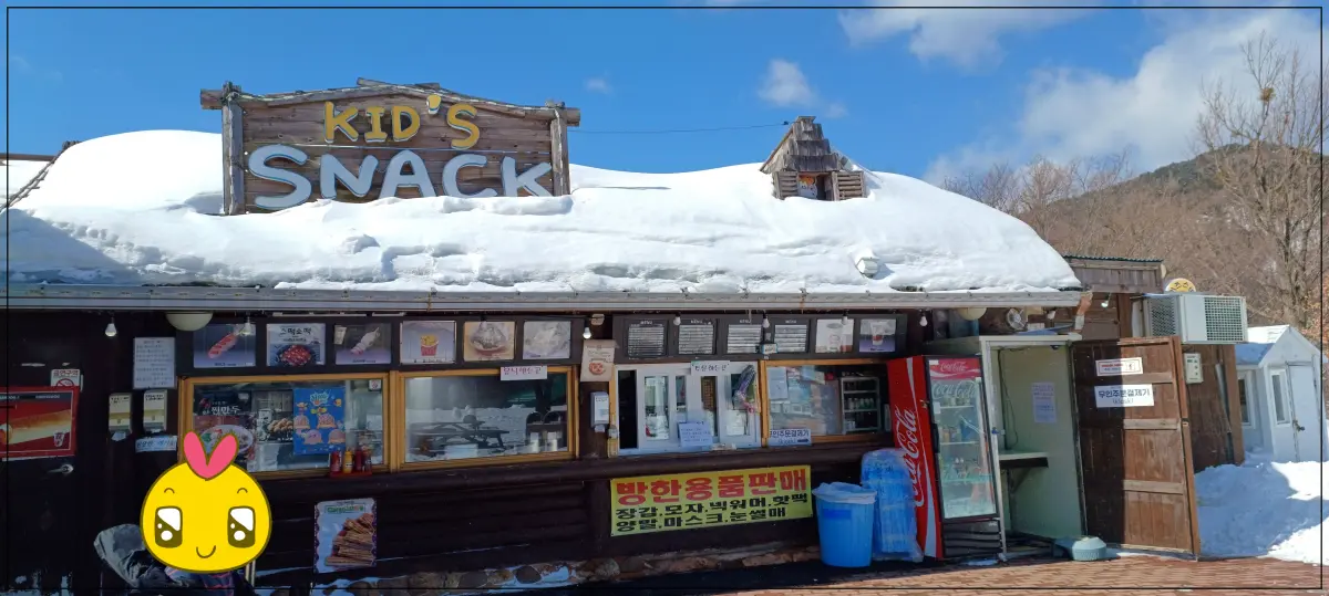 키즈스낵이라고-써있는-매점이-있음-매점지붕에-눈이-가득-쌓여있음-방한용품도-팔고-외부에-음료수-냉장고가-나와-있음