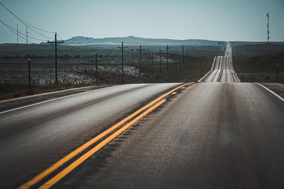 A scenic highway stretches through rolling hills lined with telephone poles and open skies.