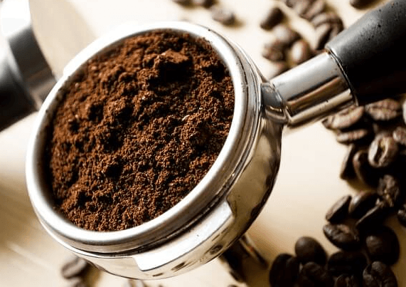 커피 홀더에 원두커피 찌꺼기가 가득 담겨있고 탁자에는 원두콩들이 뿌려져 있다.