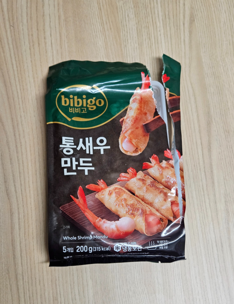 비비고 통새우 만두 제품의 앞면 포장지 사진으로 새우 비주얼이 강조된 패키지가 테이블 위에 놓여 있음