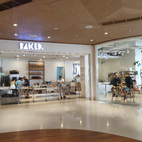 흰색 바탕 BAKED 간판, 전념 유리 안쪽 카페, 굿즈와 사람들이 보인다.