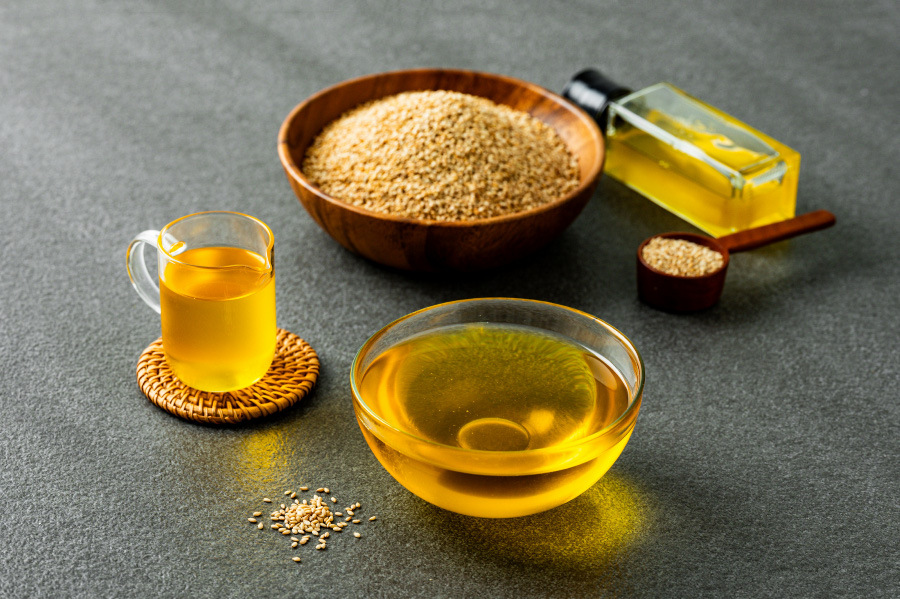 검은 바닥 위에 들깨를 가득 담은 고동색 나무 그릇을 두고 그 옆에 들기름을 가득 담은 유리병을 눕혀두고 그 밑에 들깨를 가득 담은 나무 숟가락, 그리고 그 밑과 옆에 들기름을 가득 담은 투명한 컵과 그릇을 두고 찍은 사진